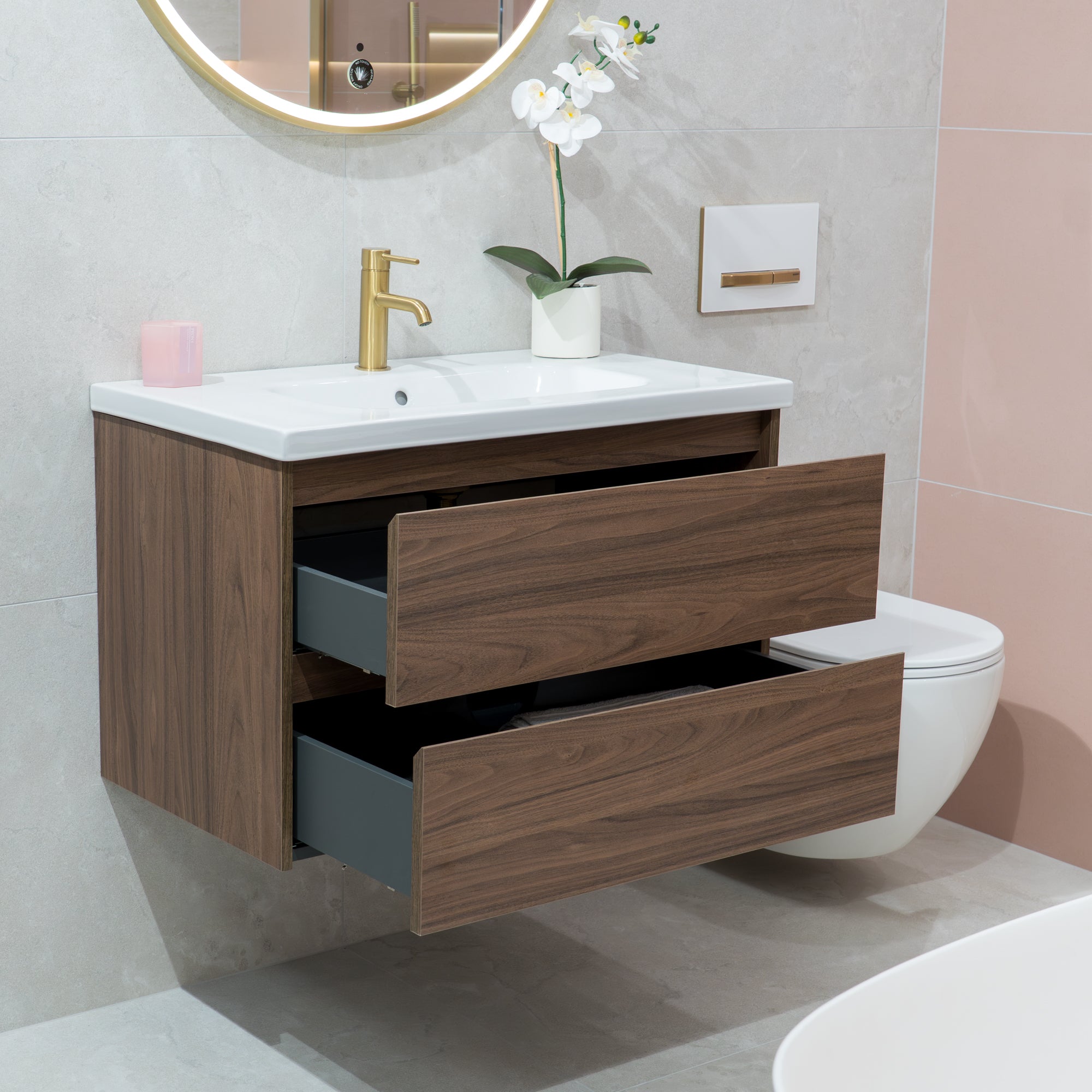 Bathroom vanity with wooden cabinet, white sink, and toilet in a modern bathroom setting.