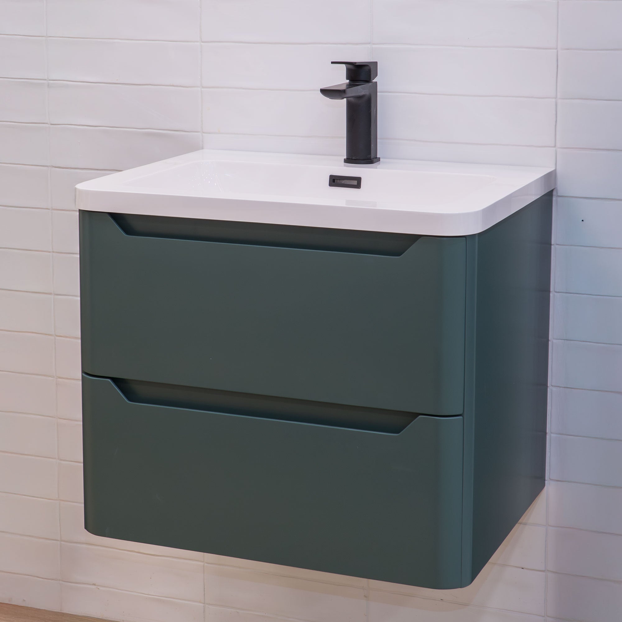 Green vanity unit with white countertop and black mixer against a tiled bathroom wall.