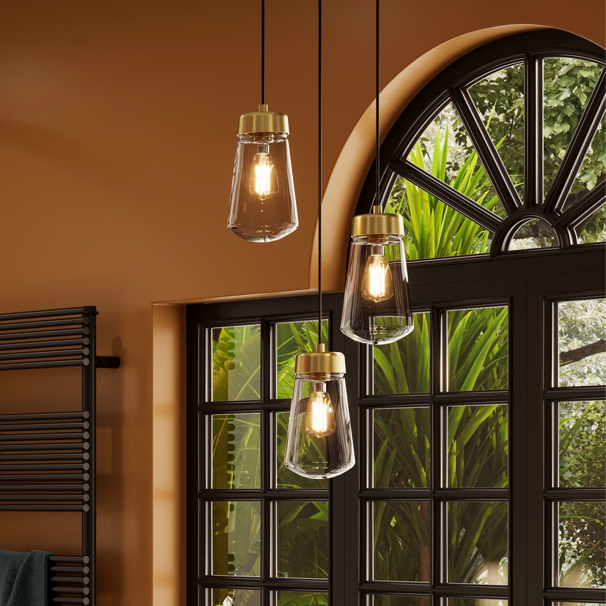 Hib summit brushed brass three hanging pendant lights with glass shades in a room with a window and plant.