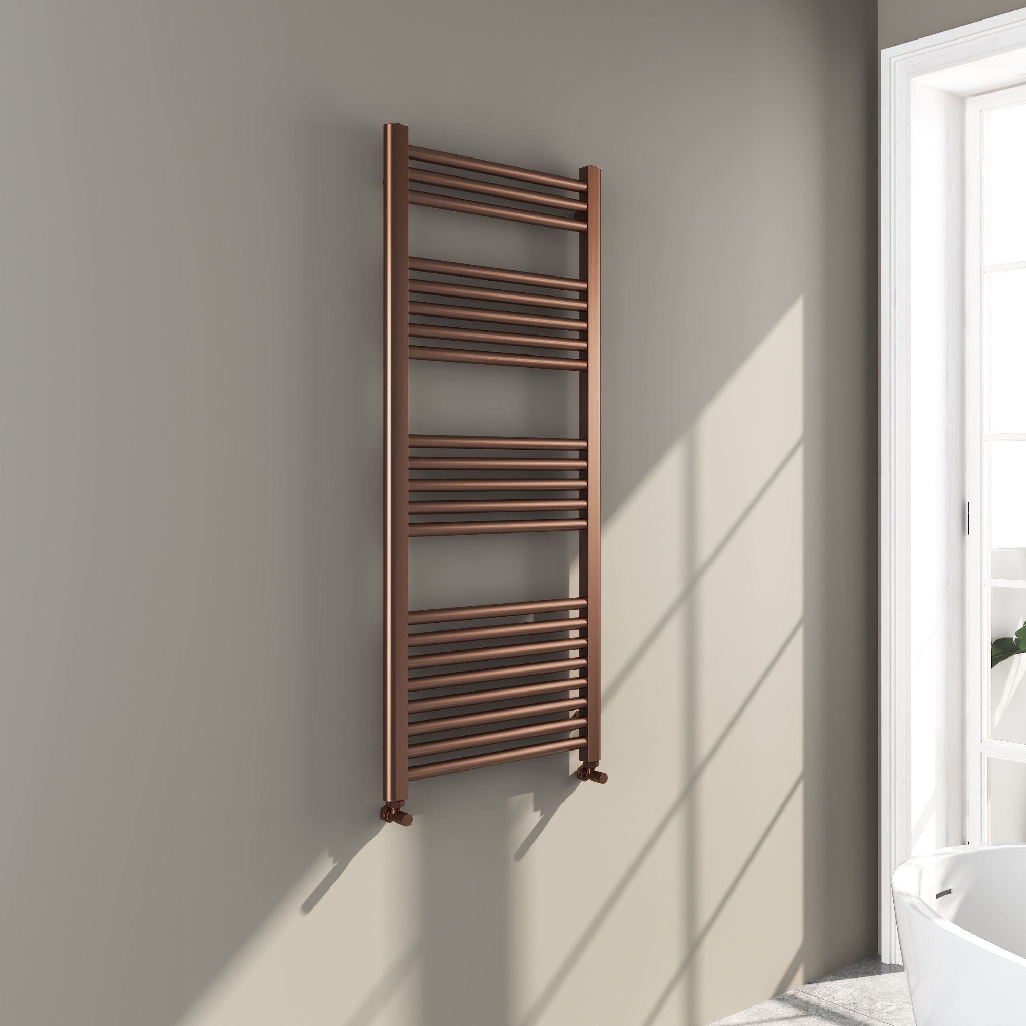 Soho brushed bronze 1200x500mm towel radiator on a gray wall with a window in the background deluxe bathrooms
