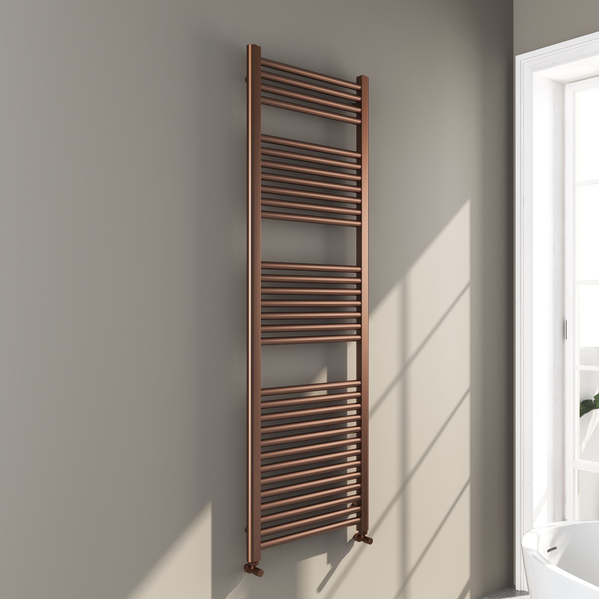 Soho brushed bronze 1600x500mm towel radiator on a gray wall with a window in the background deluxe bathrooms