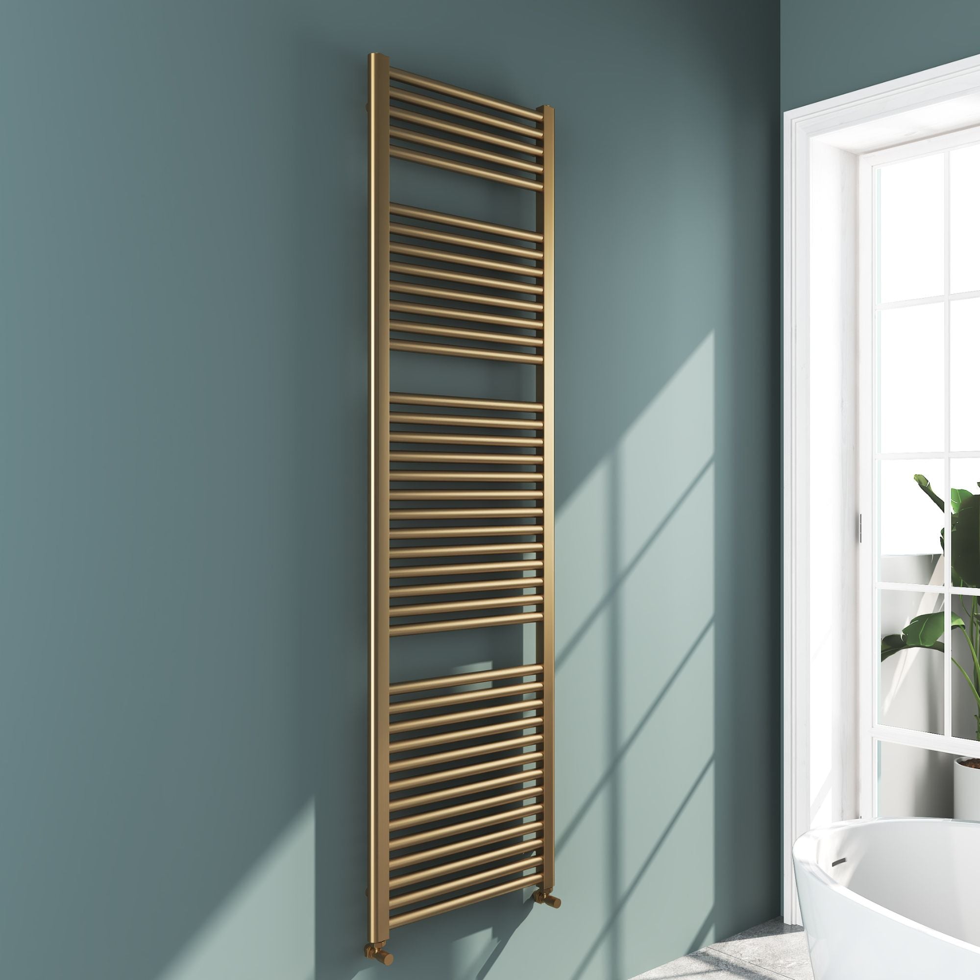 Soho brushed brass 1800x500mm towel radiator on a light blue wall with a window in the background deluxe bathrooms